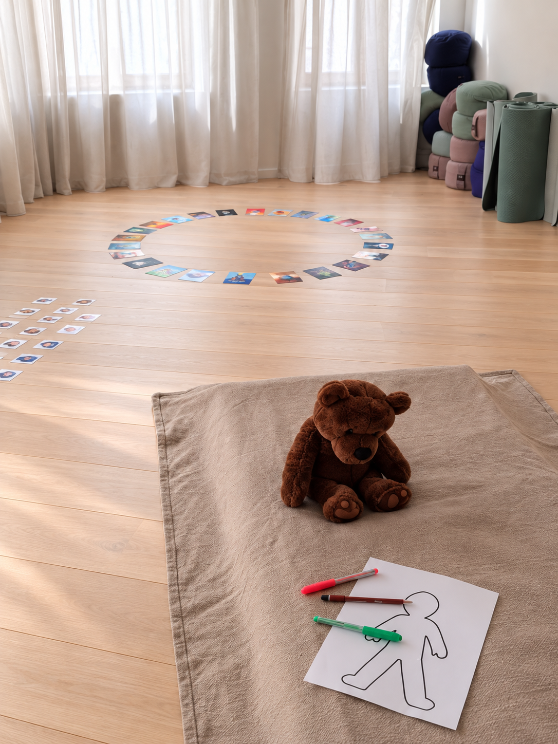 Sfeerbeeld van de praktijkruimte voor kinderen, met een knuffel, gevoelskaarten en een tekenoefening op een zachte deken
